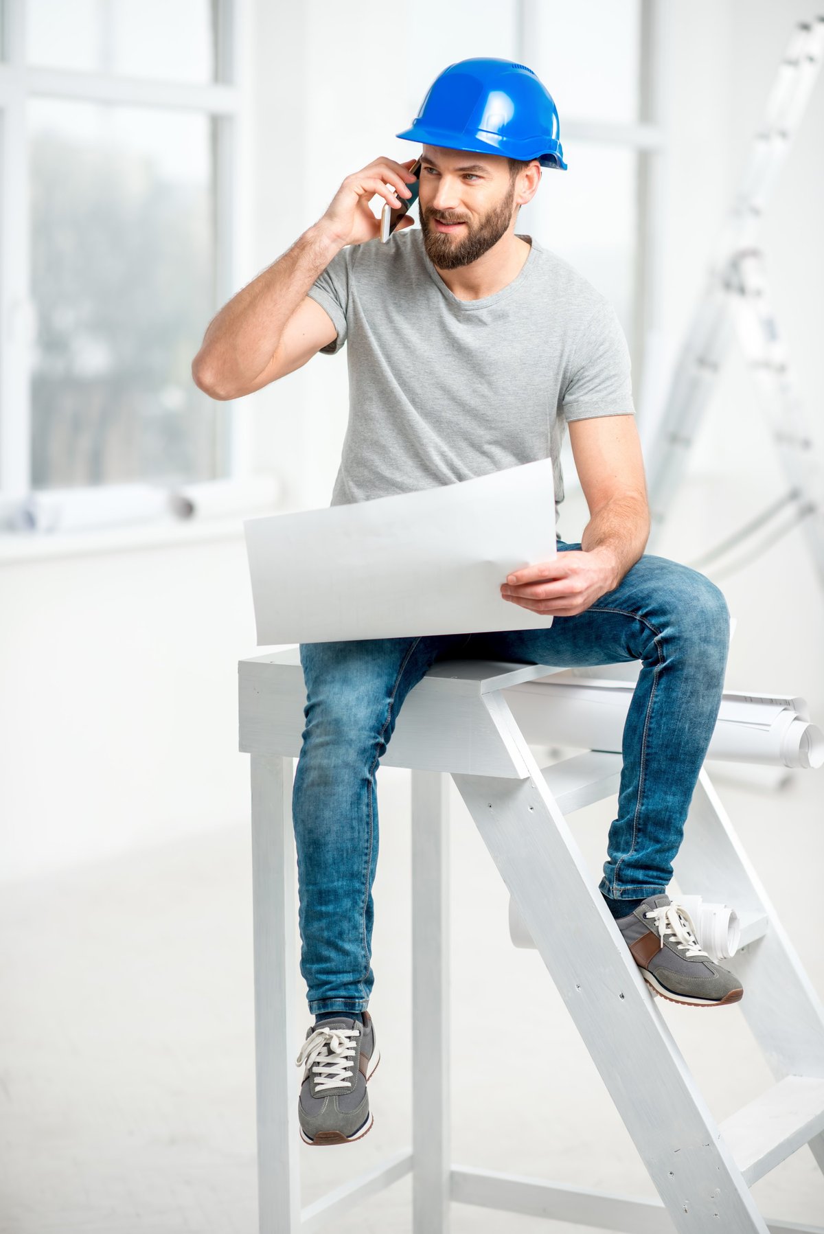 Builder repairman in helmet working with drawings and phone on renovation