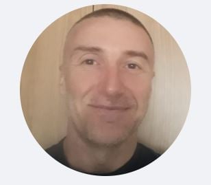 Circular profile photo of a smiling man with short blonde hair wearing a dark colored shirt